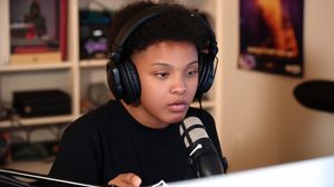 Young person with headphones and mic in a cozy bedroom, actively engaging with their digital content creation.