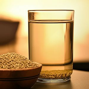 Warm Jeera water with whole cumin seeds in a glass, next to a bowl of cumin seeds.