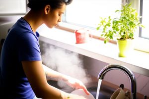Person mindfully washing dishes in a sunlit kitchen, finding peace in an ordinary task.