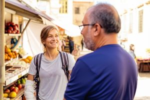 Traveler smiling and chatting with a local vendor in a European market, embracing spontaneity.
