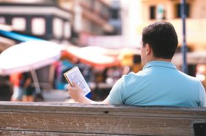 Solo traveler contemplating in a foreign city park, notebook in hand, surrounded by local life.