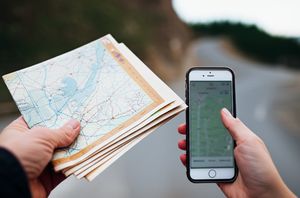Hand holding a paper map next to a smartphone map, symbolizing navigation and resourcefulness in solo travel.