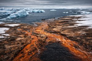 Orange 'rusting' rivers flowing through thawing Arctic permafrost into a dark, open ocean with melting ice.